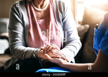 Tröstet sie in ihrer Zeit der Not. Eine Krankenschwester hält eine ältere Frau Hände in Trost. Stockfoto