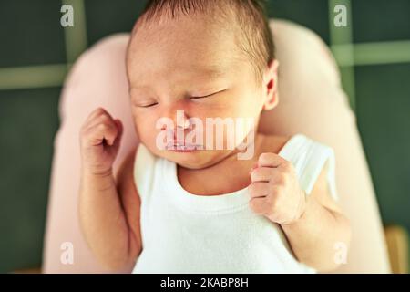 Ein müder kleiner Junge schläft mit geschlossenen Augen, während seine Mutter ihn zu Hause in den Händen hält. Stockfoto