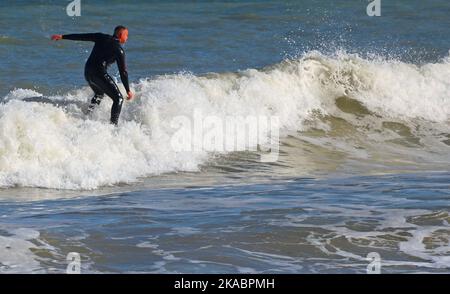 Mann, der eine Welle im Meer surft. Stehen auf einem Surfbrett, das auf dem weißen Kamm einer Welle reitet. Stockfoto