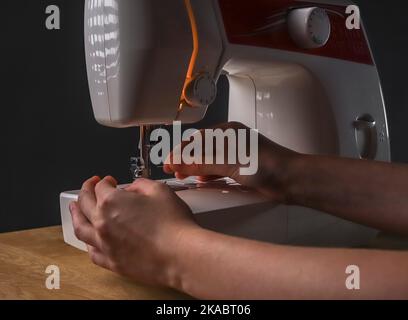Schneiderhände führen Faden durch Nadelloch in der Nähmaschine, Arbeit beginnen. Stockfoto