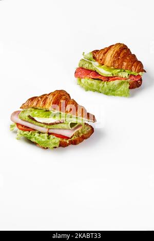 Zwei Croissant-Sandwiches, gefüllt mit Spiegeleiern, Schinken, Salami, Käse, gesalzenem Lachs und Gemüse Stockfoto