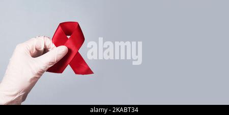 Roter Bandbogen für AIDS- und HIV-Aufklärungstag in den Händen der Ärzte. Medizinisches Banner mit Platz für Text. Stockfoto