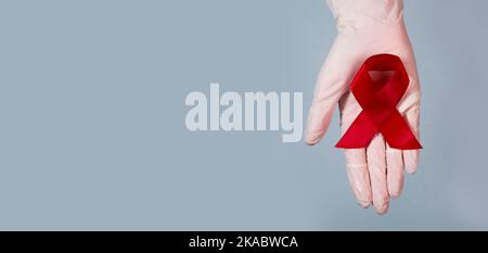 Roter Bandbogen für AIDS und HIV-Bewusstsein in den Händen. Medizinisches Banner mit Kopierbereich. Stockfoto