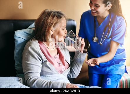 Eine Krankenschwester, die einem Patienten Medikamente und ein Glas Wasser gibt. Stockfoto