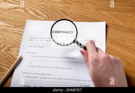 Papiervertrag auf Holztisch mit Lupe in weiblicher Hand. Stockfoto