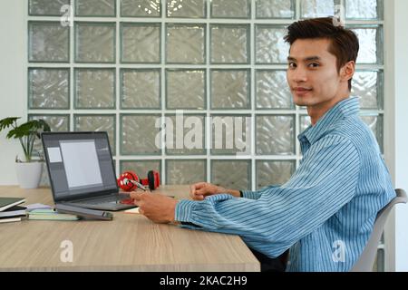 Gutaussehender asiatischer freier Mann, der im kreativen Bürostudio mit Filmmaterial und Sound arbeitet Stockfoto