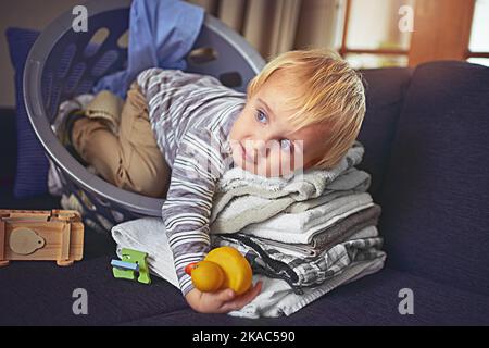 So weich fühlt es sich an wie ein Teddybär. Ein entzückender kleiner Junge rollte sich mit einem Korb voller sauberer Wäsche zusammen. Stockfoto