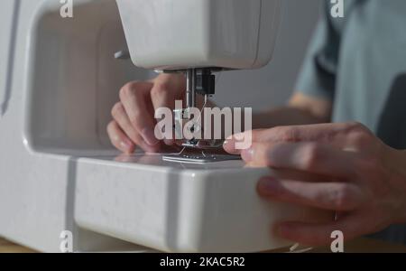 Weibliche Hände, die Faden durch das Nadelloch in der Nähmaschine einführen, Nahaufnahme. Stockfoto