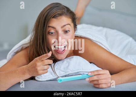 Junge Brünette Frau mit Schwangerschaftstest im Bett Stockfoto