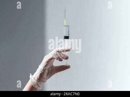 Spritze mit Nadel in den Ärzten Hand in Handschuh über Hintergrund mit Tageslicht und Schatten. Stockfoto