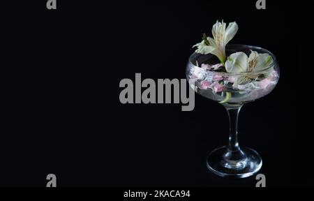 Glas mit Wasser und weißen, rosa Blüten auf schwarzem, isolierten Hintergrund. Werbung für Parfums und Cremes. Hochwertige Fotos. Stockfoto