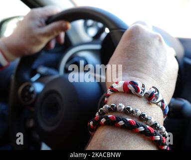 Die Hände eines Mannes mit roten, weißen, blauen Armbändern, der ein Auto steuert Stockfoto