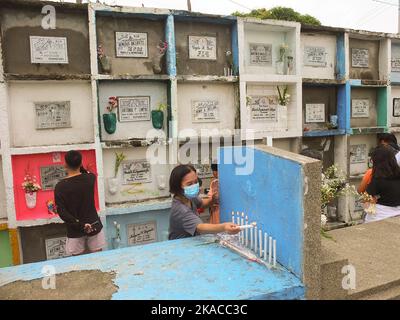 Caloocan City, Philippinen. 01.. November 2022. Eine Frau zündet während des Allerheiligen-Tages Kerzen am Grab ihres verstorbenen Verwandten an. Filipinos strömen nach zwei Jahren der Covid-19-Pandemie auf Friedhofs, da sich die Einschränkungen langsam lockern. Die Tradition, Blumen zu bringen, Kerzen anzuzünden und sogar Nahrung an der Begräbnisstätte ihrer verstorbenen Lieben anzubieten. Kredit: SOPA Images Limited/Alamy Live Nachrichten Stockfoto