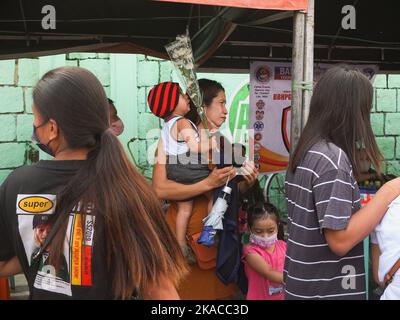 Caloocan City, Philippinen. 01.. November 2022. Ein Kind starrt auf einen Blumenstrauß, der von seiner Mutter während Allerheiligen gehalten wird. Filipinos strömen nach zwei Jahren der Covid-19-Pandemie auf Friedhofs, da sich die Einschränkungen langsam lockern. Die Tradition, Blumen zu bringen, Kerzen anzuzünden und sogar Nahrung an der Begräbnisstätte ihrer verstorbenen Lieben anzubieten. Kredit: SOPA Images Limited/Alamy Live Nachrichten Stockfoto