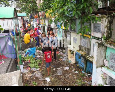 Caloocan City, Philippinen. 01.. November 2022. Die Besucher des Friedhofs laufen entlang eines Müllstapels, um ihren Toten während des Allerheiligen-Tages ihre Achtung zu erweisen. Filipinos strömen nach zwei Jahren der Covid-19-Pandemie auf Friedhofs, da sich die Einschränkungen langsam lockern. Die Tradition, Blumen zu bringen, Kerzen anzuzünden und sogar Nahrung an der Begräbnisstätte ihrer verstorbenen Lieben anzubieten. Kredit: SOPA Images Limited/Alamy Live Nachrichten Stockfoto