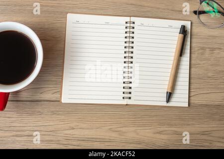 Leeres Notizbuch, schwarze Kaffeetasse und Stift auf Holztisch, Ansicht von oben und Platz zum Kopieren. Frohes neues Jahr, Ziele, Auflösung, To-Do-Liste, Strategie und Plan Konz Stockfoto