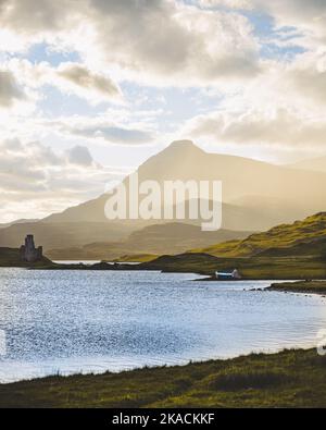 Nebel verschlingt einen Berg in den schottischen Highlands neben einem großen Loch mit einem malerischen kleinen Schloss am Ufer. Stockfoto