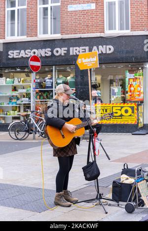 Irland Irland Irland Dublin Anne Street South Leila Jane Keeney lizenzierte Busker Solo junger Musiker Gitarre singen spielen Mikrofon Zeichen Schilder Taschen Trolley Stockfoto