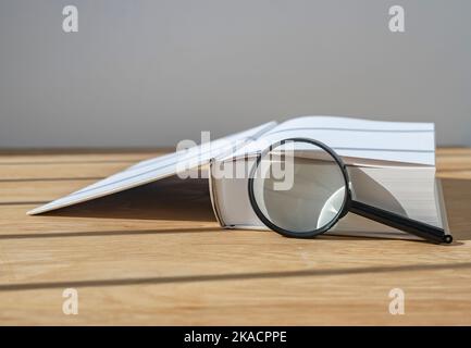 Lupe mit offenem dickem Buch auf Holzschreibtisch mit Tageslicht. Stockfoto