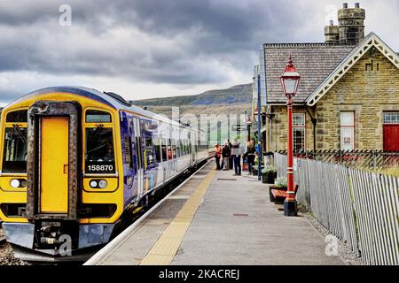 Passagiere, die Schlange stehen, um am Bahnhof Ribblehead auf der Linie Settle nach Carlisle, Ribble Valley, North Yorkshire, England, Großbritannien, in einen Zug zu steigen Stockfoto