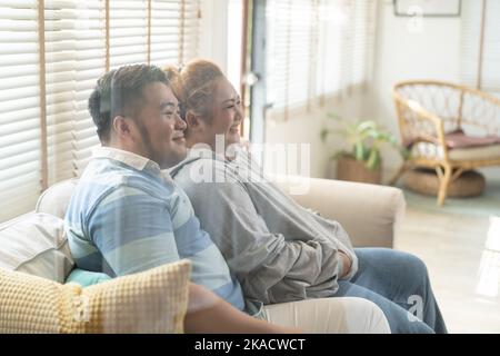Junge asiatische mollige Paar Fernsehen-Serie und Film auf der Couch im Wohnzimmer. Mann und Frau genießen eine lustige Zeit zusammen zu Hause. Die Menschen lachen und lächeln zusammen Stockfoto