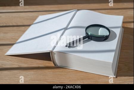 Lupe mit offenem dickem Buch auf Holzschreibtisch mit Tageslicht. Konzept von Grund auf neu beginnen. Stockfoto