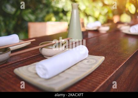 Japanisches Restaurant in traditionellem Stil, leerer Teller auf Matte in der Nähe des Essstäbchen-Behälters, Selective Focus Stockfoto