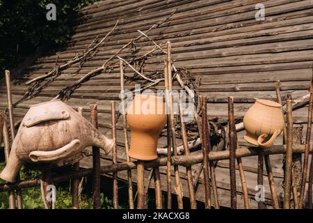 Alte Tontöpfe hängen einfach an einem Weidenzaun. Ukrainische ethnische Gerichte, traditionelle Kultur der Ukraine Stockfoto