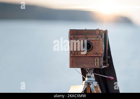 Alte Holzkamera. Alte Kamera auf einem Stativ. Sonnenuntergang am Meer Stockfoto