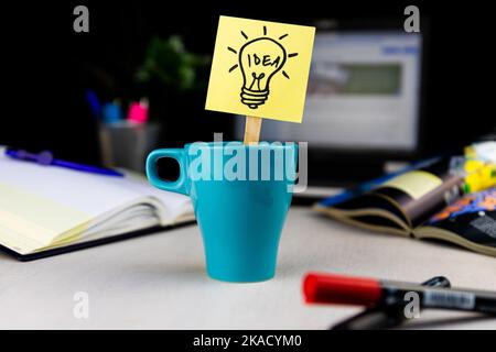Glühbirnendudel auf Haftnotiz in einer Tasse Kaffee am Schreibtisch gezeichnet. Ideen, Inspiration und kreatives Denken kommen mit einer morgendlichen Tasse Stockfoto