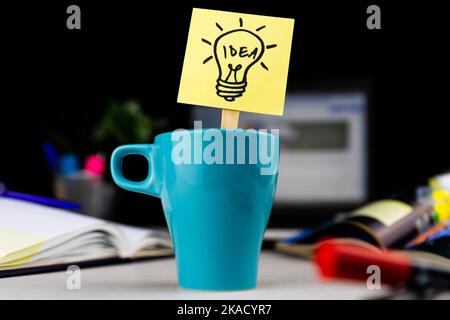 Glühbirnendudel auf Haftnotiz in einer Tasse Kaffee am Schreibtisch gezeichnet. Ideen, Inspiration und kreatives Denken kommen mit einer morgendlichen Tasse Stockfoto