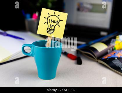 Glühbirnendudel auf Haftnotiz in einer Tasse Kaffee am Schreibtisch gezeichnet. Ideen, Inspiration und kreatives Denken kommen mit einer morgendlichen Tasse Stockfoto