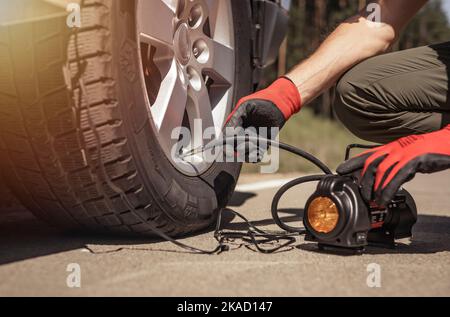 Reifenpumpe, die das Autorad aufpumpt. Reifenaufblasvorrichtung in Menschenhand mit Manometer. Stockfoto