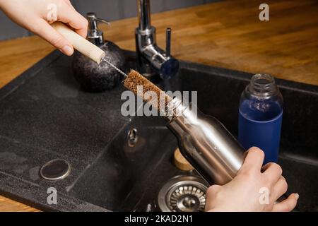 Waschen Reinigung wiederverwendbare Trinkflasche mit Kokosfaser-Fläschchenreinigungsbürste in der heimischen Küche. Nachhaltiges Lifestyle-Konzept. Stockfoto