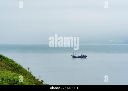 Fischerboot auf See vor dem Hintergrund einer weit entfernten nebligen Küste Stockfoto