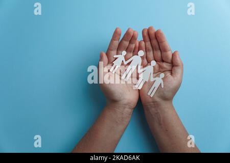 Hände mit Papier Familienausschnitt, Lebensversicherung, soziales Distanzierungskonzept, covid19, auf blauem Hintergrund, Familienschutz Stockfoto