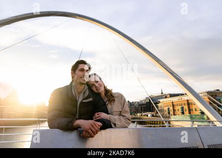 Eine Weitwinkelaufnahme eines jungen Paares, das Seite an Seite steht und die Aussicht auf einer Brücke in der Stadt zusammen betrachtet, sind sie verliebt. Stockfoto