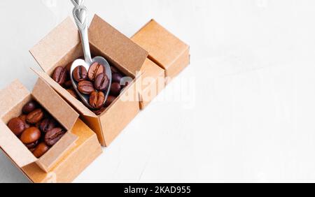 Nehmen Sie dunkle geröstete Kaffeebohnen mit einem kleinen Teelöffel aus Miniatur-Kartons isoliert auf weißem Hintergrund. Testkonzept für die Kaffeequalität. Stockfoto