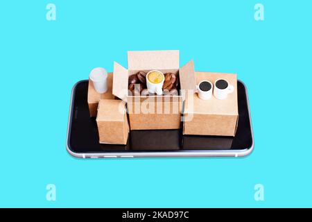 Kaffee liefert e-Commerce-Setup: Kleine Kartons mit gerösteten Kaffeebohnen und Kaffeetassen auf einem Smartphone isoliert auf blau platziert. Stockfoto