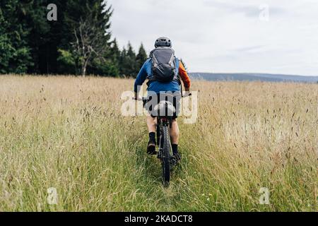 Bikepacking in den Bergen. Mann, der mit seinem Fahrrad und Rucksack auf einer Wiese steht, bereit für eine Bikepacking-Abenteuerfahrt. Stockfoto