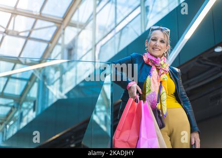 Dame mit Einkaufstaschen lächelt fröhlich und schaut vor einem Geschäft zur Kamera. Weihnachtseinkäufe. Stockfoto