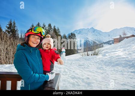 Mutter hält ein kleines Mädchen im Skioutfit über den Bergen Stockfoto