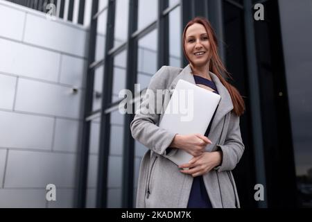 Eine rothaarige Geschäftsfrau geht mit einem Laptop zur Arbeit Stockfoto