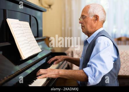 Großvater lernt zu Hause Klavier zu spielen. Leben nach dem Ruhestand Konzept Stockfoto