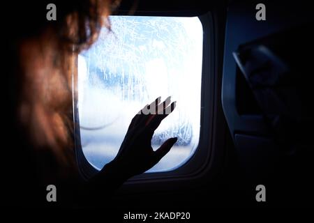 Weibliche Hand berührt die warmen Sonnenstrahlen vom Flugzeugfenster. Frau freut sich auf die Reise in ihren Urlaub. Mädchen auf einer Reise Flug sitzen in Stockfoto