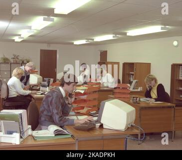 Etwa 1989, historisches Großraumbüro, männliche und weibliche Mitarbeiter, die an Schreibtischen arbeiten, einige am Telefon und mit Computerterminals der Epoche, England, Großbritannien. Stockfoto