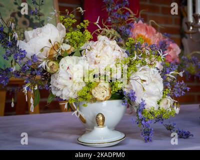 Blumenarrangements im barocken Stil in einer weißen Porzellanvase auf dem Tisch. Weiße und pinkfarbene Pfingstrosen. Stockfoto