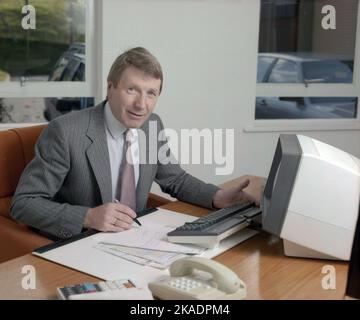 1989, historischer, leitender Unternehmensleiter in seinem Büro, sitzend an einem Schreibtisch mit Stift und Papier auf einem Schreibtischflecker und einem kleinen Computerterminal und einer Tastatur der damaligen Zeit, England, Großbritannien. Stockfoto