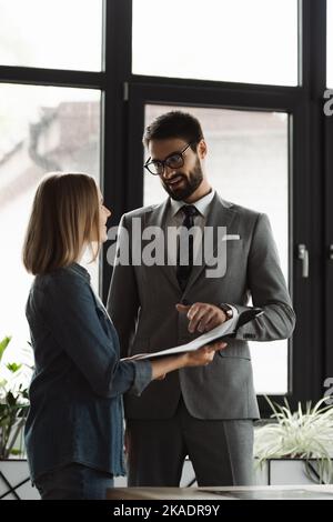 Lächelnder Geschäftsmann zeigt auf Lebenslauf in der Nähe von jungen Arbeitssuchenden im Büro, Bild Stockfoto