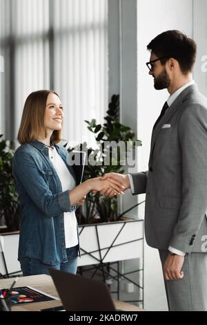 Lächelnder Arbeitssuchender hält Lebenslauf und schüttelt die Hand des Geschäftsmannes im Büro, Stockbild Stockfoto